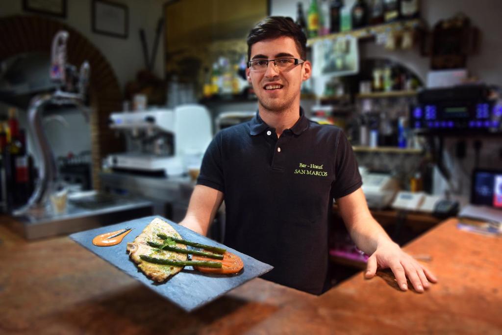 a man holding a tray of food on a counter at Pensión San Marcos in Arcos de la Frontera