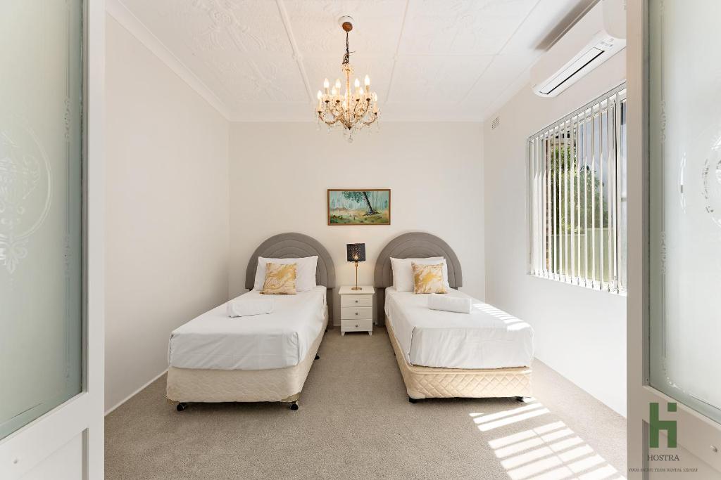 two beds in a white room with a chandelier at edgeware house in Sydney