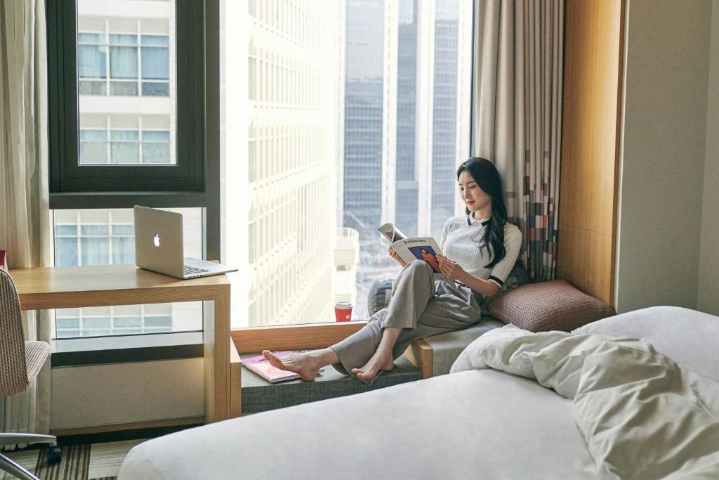 a woman sitting in a hotel room reading a book at Aloft Seoul Myeongdong in Seoul