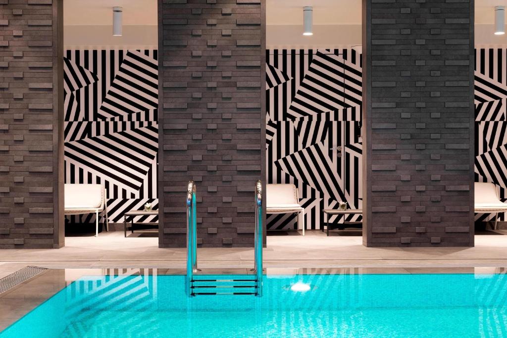 a pool with chairs and a wall with black and white tiles at Renaissance Warsaw Airport Hotel in Warsaw