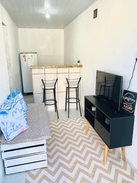 a living room with a tv and a counter with stools at Sua Kitnet a menos de 5min da Praia in Santa Cruz Cabrália