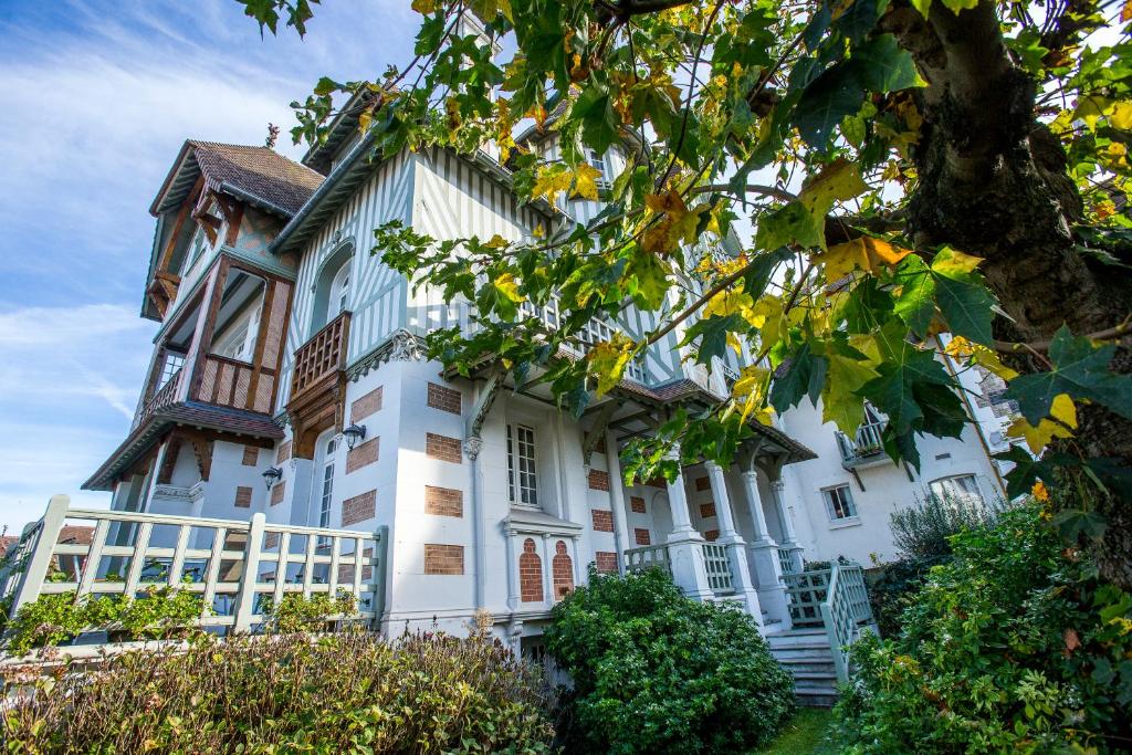a large white building with a tree in the foreground at Villa Augeval Hôtel de charme & Spa in Deauville