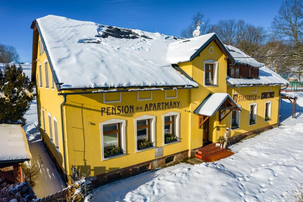 a yellow house with snow on the roof at Apartmány U Šťastných in Cerny Dul