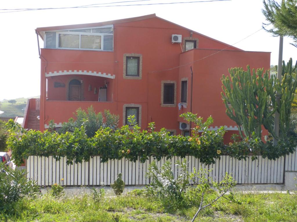 a red house behind a white fence with plants at B&B Figli Dei Fiori in Realmonte