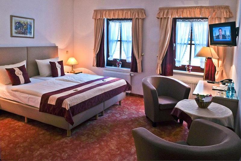 um quarto com uma cama, uma cadeira e janelas em Altstadthotel "Garni" Grimma em Grimma