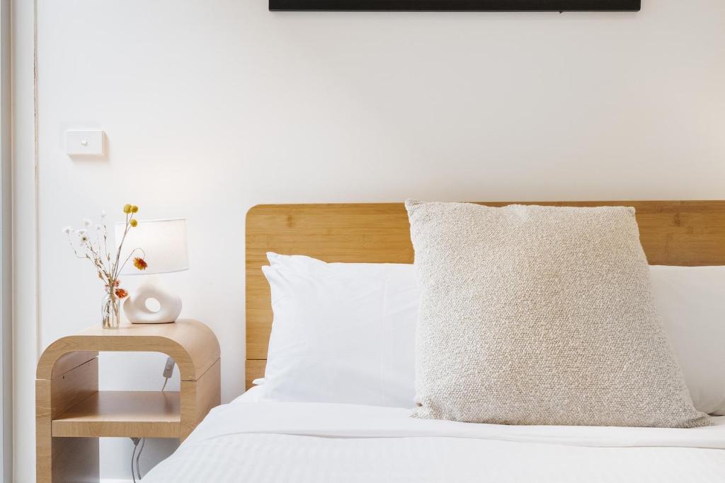 un lit avec des draps blancs et une tête de lit en bois dans l'établissement StayCentral - Brunswick Boutique, à Melbourne