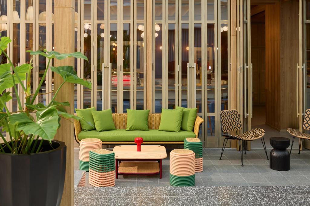 A bright communal seating area with a green sofa, colorful stools, plants, and patterned chairs.