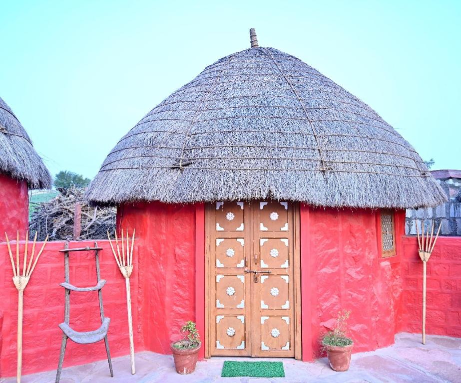 a red hut with a thatched roof and a chair at Gangaram osian village home stay in Osiān