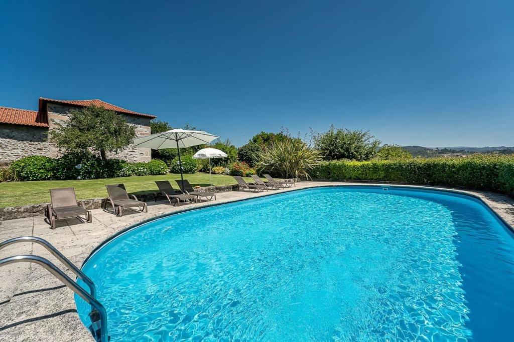 a large swimming pool with chairs and an umbrella at Casa do Lagar in Cabeceiras de Basto