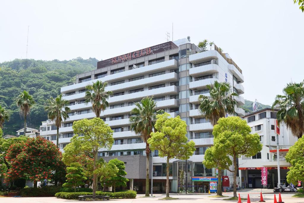 a tall white building with palm trees in front of it at Hotel Sunmi Club in Atami