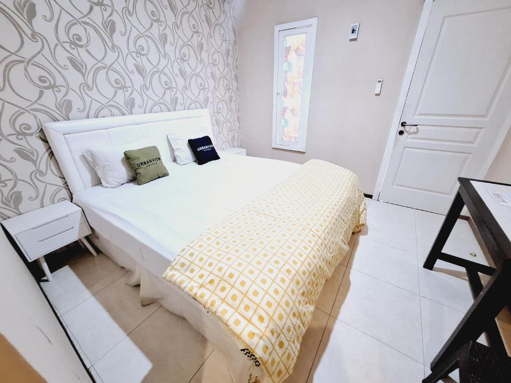 a bedroom with a white bed with a yellow blanket at Urbanview Roemah Tanjung Blitar in Blitar