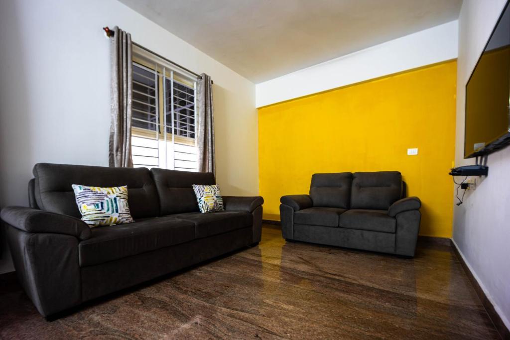 a living room with two black couches and a yellow wall at HRBR Enclave one BHK with fully furnished in Bengaluru