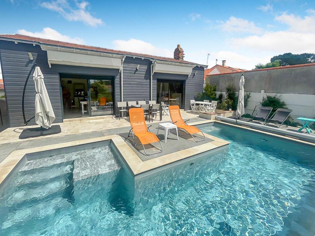 einen Pool mit zwei orangenen Stühlen, einem Tisch und Stühlen in der Unterkunft Piscine privée proche Thalassothérapie et Mer in Pornic