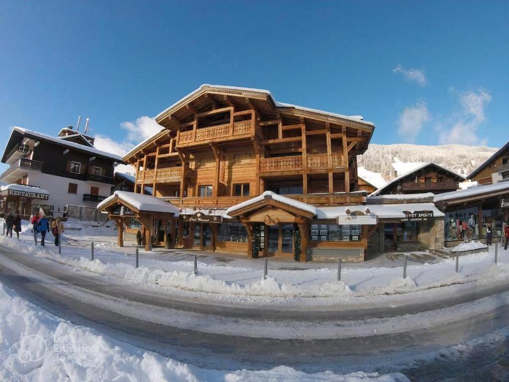 un grand bâtiment en bois avec de la neige au sol dans l'établissement Appartement 2 Chambres Residence Le Mont Chéry Au Pied des Pistes Plein Centre, aux Gets