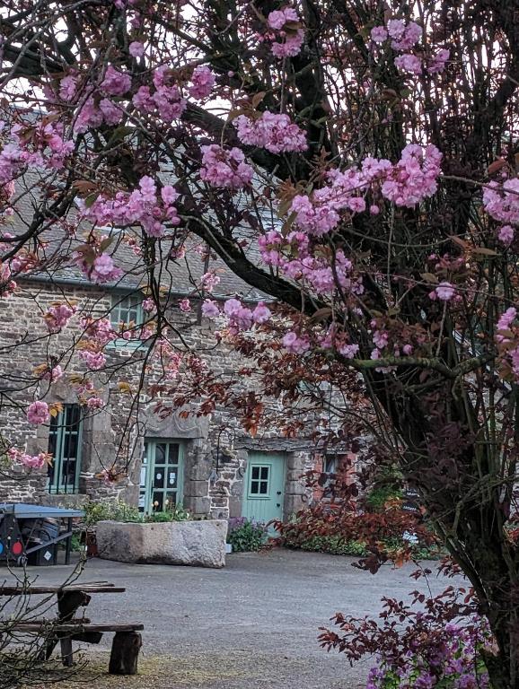 un bâtiment en pierre avec des fleurs roses devant lui dans l'établissement ferme de la gortiere, à Le Teilleul
