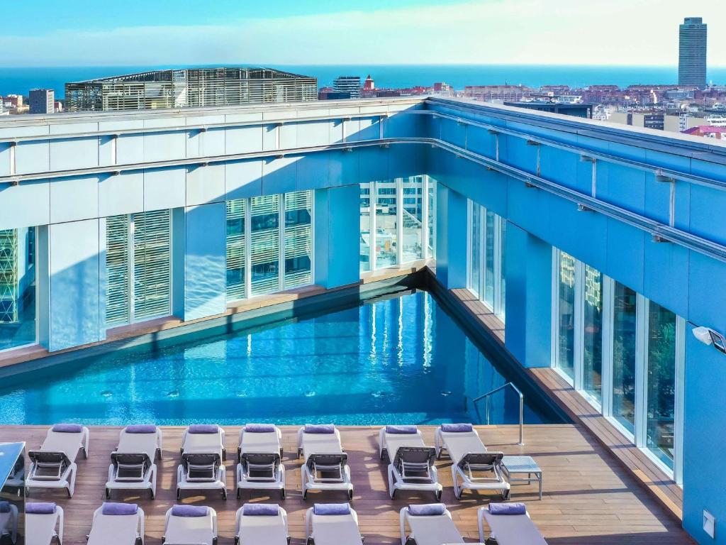 a swimming pool on the roof of a building with lounge chairs at Novotel Barcelona City in Barcelona