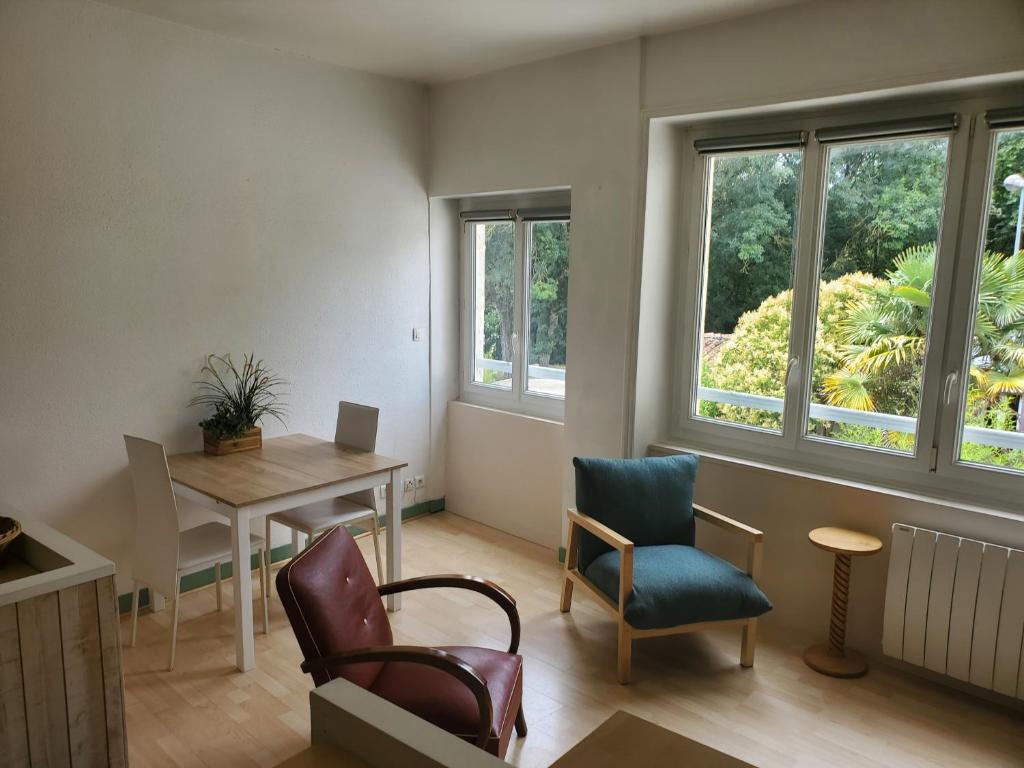 un salon avec une table, des chaises et des fenêtres dans l'établissement L'Appart sur Jardin 42m2 très calme, à La Rochelle