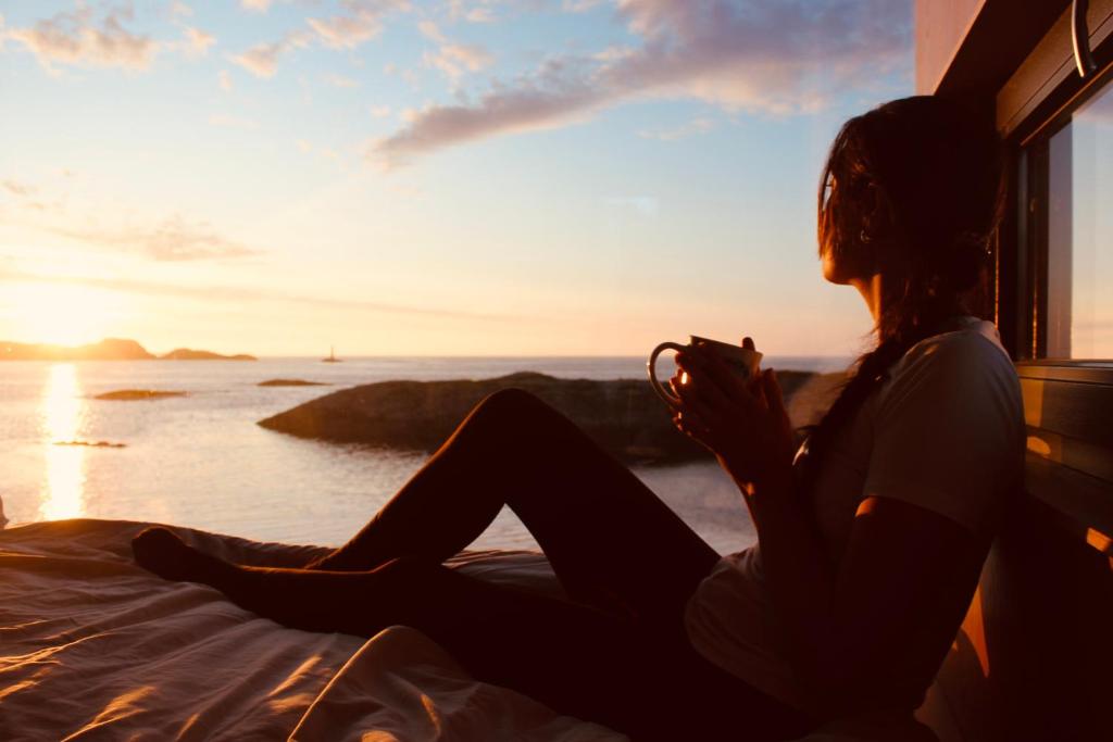 a woman sitting on a bed looking out a window at the ocean at Atlantic Road Sleeping Experience Re-Treats in Vevang