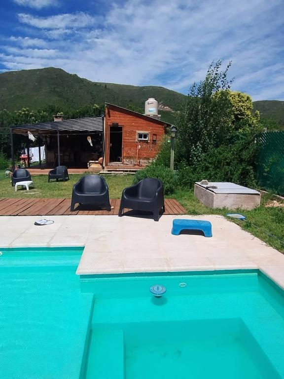 a swimming pool with two chairs and a house at Aldea La Abundancia Cabaña Hostel in La Falda