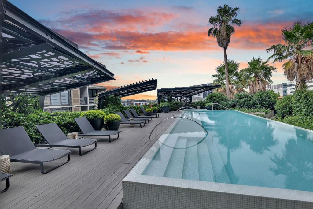 a pool on the roof of a building with chairs and a sunset at North Melbourne Retreat in Melbourne