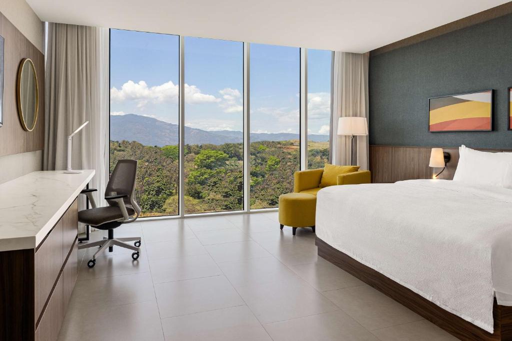 a hotel room with a bed and a chair and windows at Hilton Garden Inn San Jose Airport City Mall in Alajuela City
