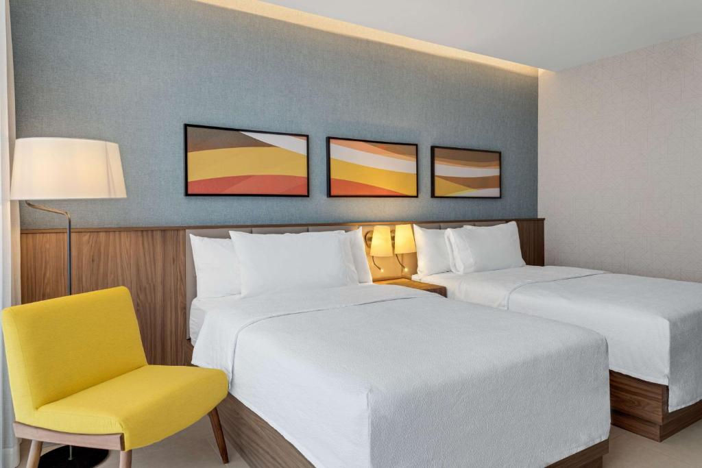 a hotel room with two beds and a yellow chair at Hilton Garden Inn San Jose Airport City Mall in Alajuela City