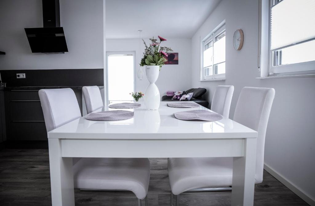 a white dining room table with white chairs and a vase with flowers at BraWa FeWo Erlebnis Region Europa Park Schwarzwald Badespaß Rulantica in Ettenheim
