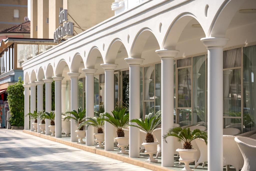 a building with white columns and potted plants on a street at Hotel Croce di Malta e Mexico in Cesenatico
