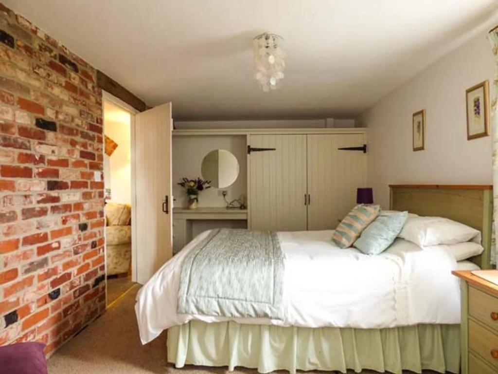 a bedroom with a white bed and a brick wall at Woodman's Barn with countryside views - Sleeps 6 in Norwich