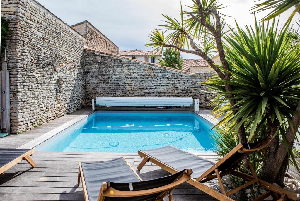 une piscine avec deux chaises et un banc à côté d'un mur de briques dans l'établissement Île de Ré - 9 personnes - Plage à pieds - Piscine, à Saint-Clément-des-Baleines