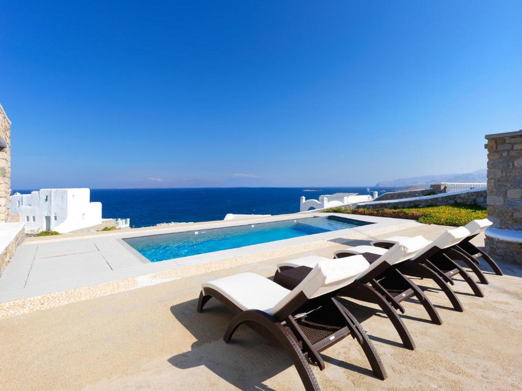 a group of chairs sitting next to a swimming pool at The Mykonian Sunset Villas - 10min from Town in Agios Ioannis Mykonos