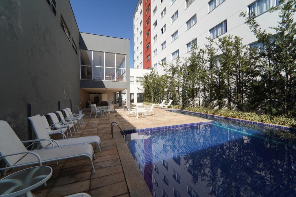 ein Schwimmbad mit weißen Stühlen und ein Gebäude in der Unterkunft Hotel Abba Uno in Betim
