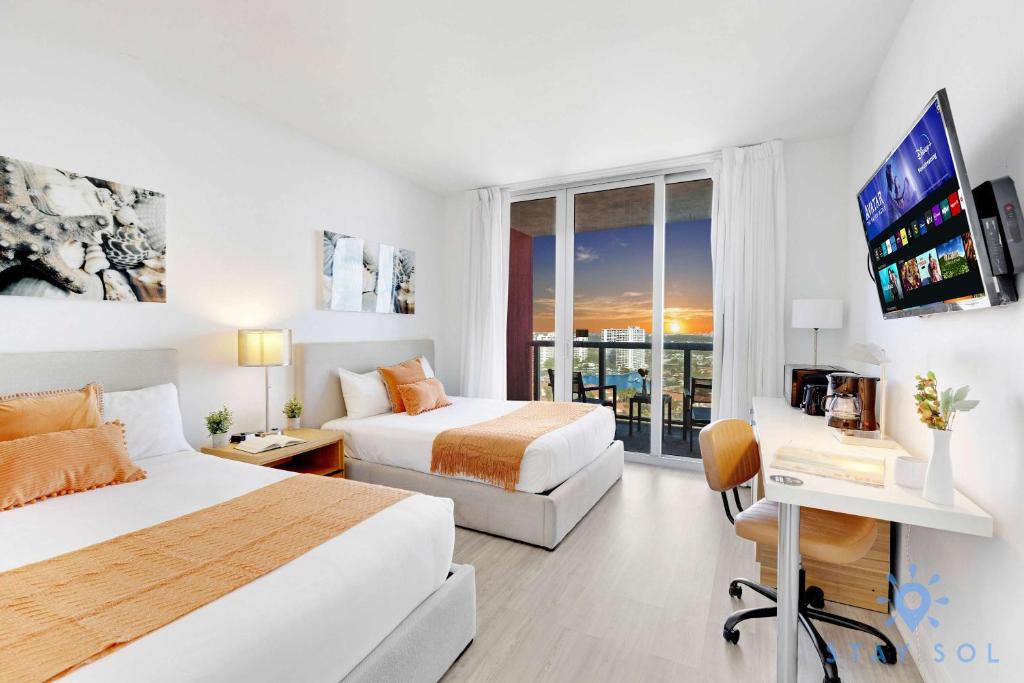 a hotel room with two beds and a flat screen tv at Amazing Balcony Near Beach in Hallandale Beach
