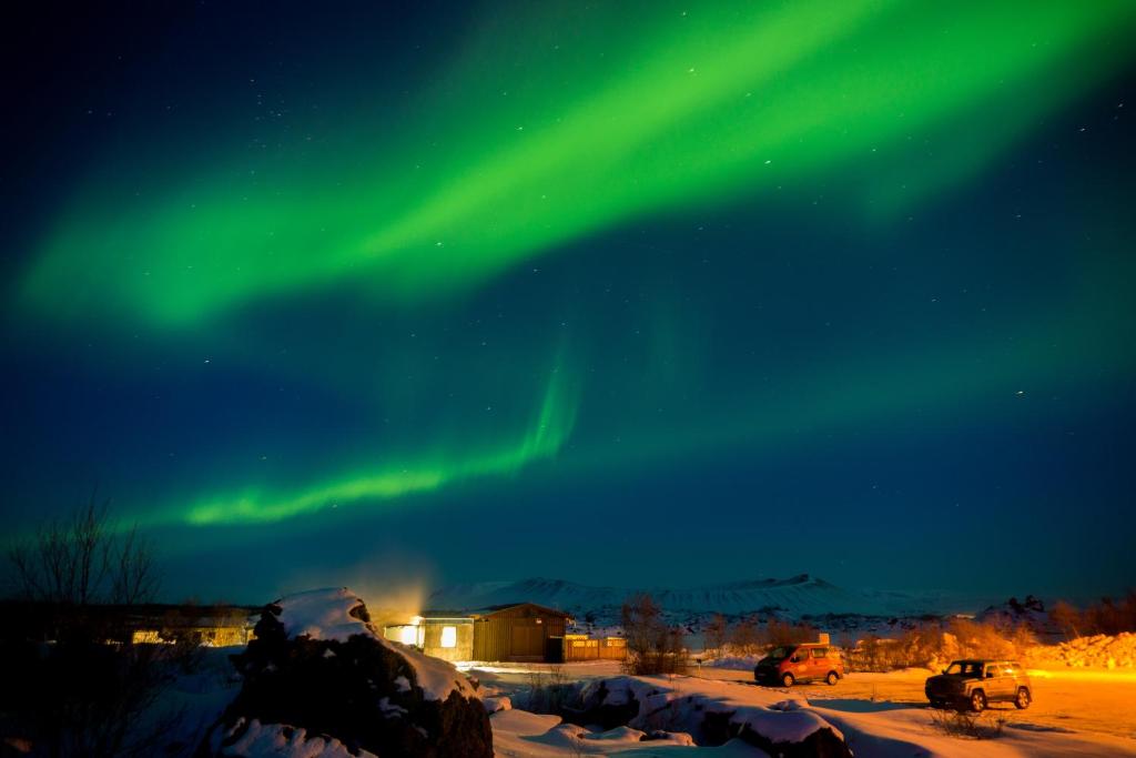 an aurora in the sky over a parking lot with cars at Vogar Travel Service in Myvatn