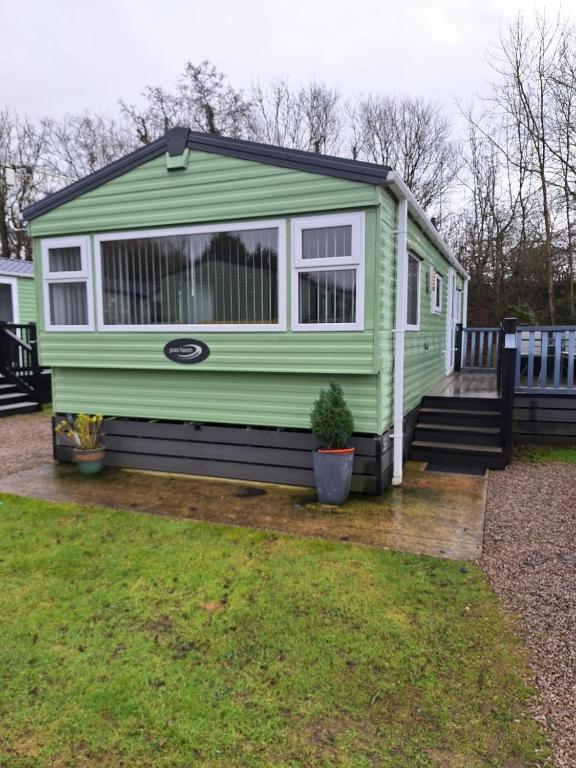 a green tiny house sitting on a wooden deck at 11 Borwick Lakes in Carnforth