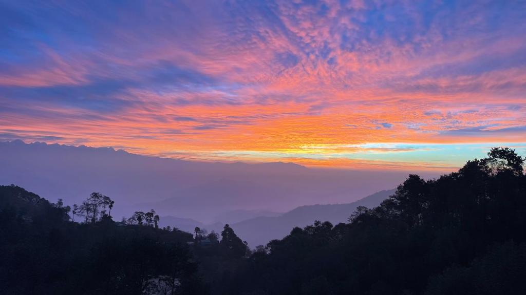 a sunset in the mountains with trees in the foreground at Hotel Everest Window View in Nagarkot