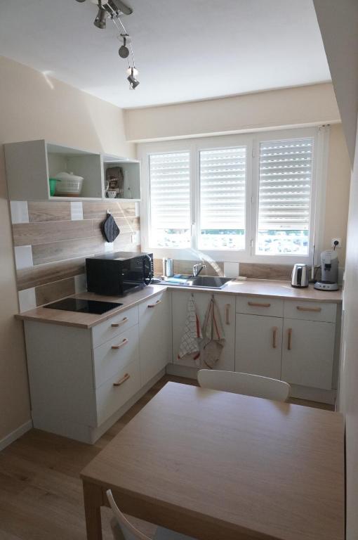 une cuisine avec des placards blancs, des fenêtres et une table dans l'établissement Appartement rénové proche de la plage, à Bénodet