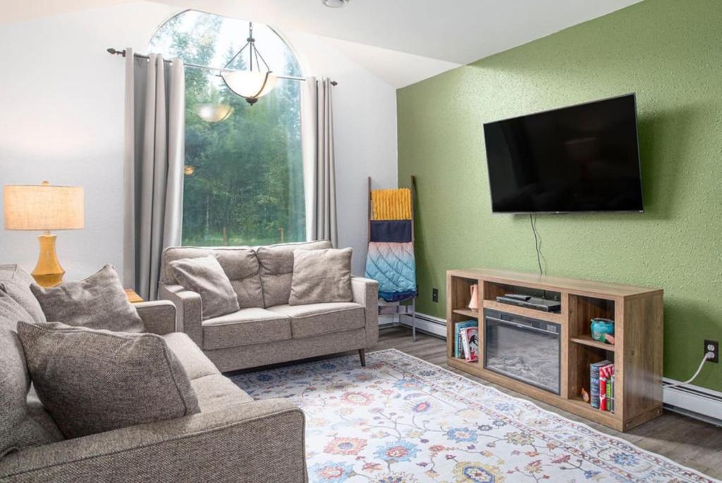 a living room with a flat screen tv on a green wall at Sunflower Sanctuary Minutes to Fairbanks in Highland Park