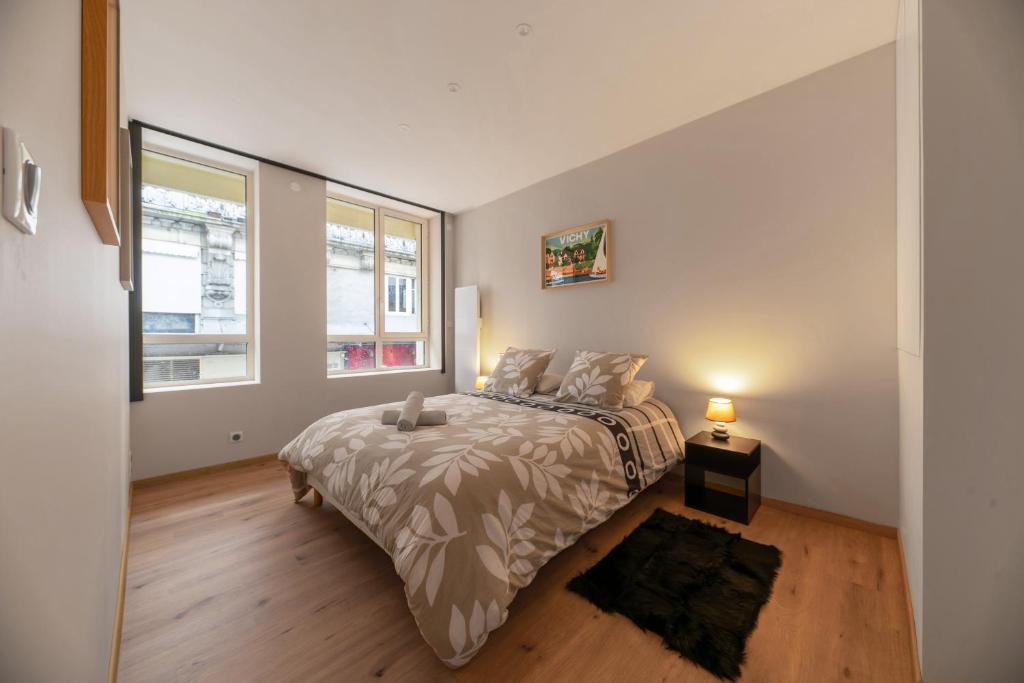 a bedroom with a bed and a lamp and two windows at L'Hotel des Postes - Appartement design en centre ville in Vichy