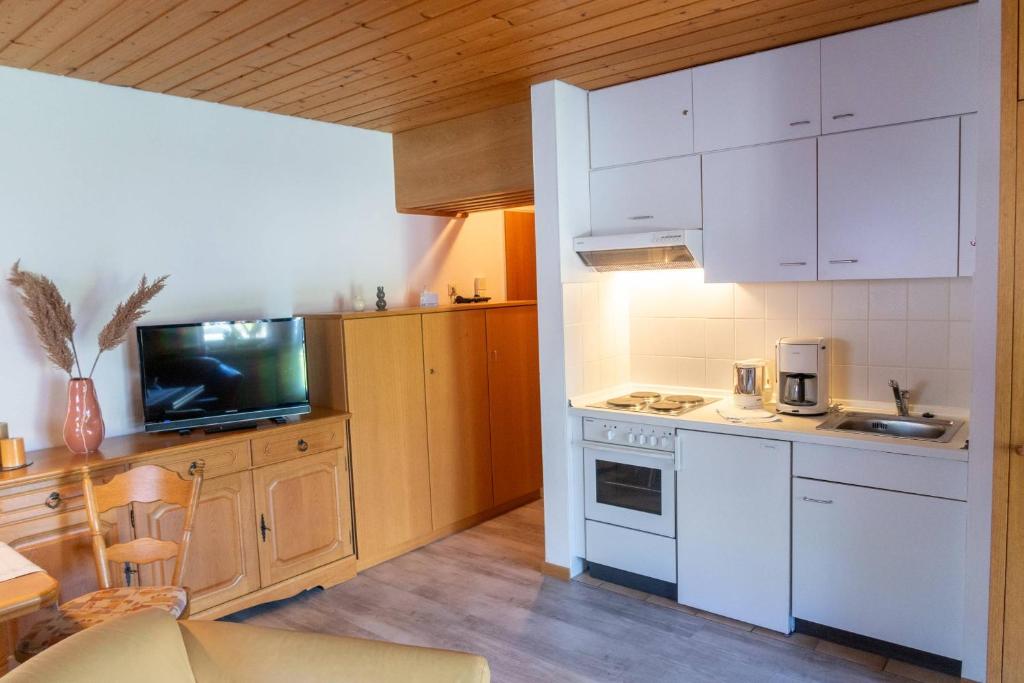 cocina con armarios blancos, fregadero y TV en Ferienwohnung Lübbers, en Reit im Winkl