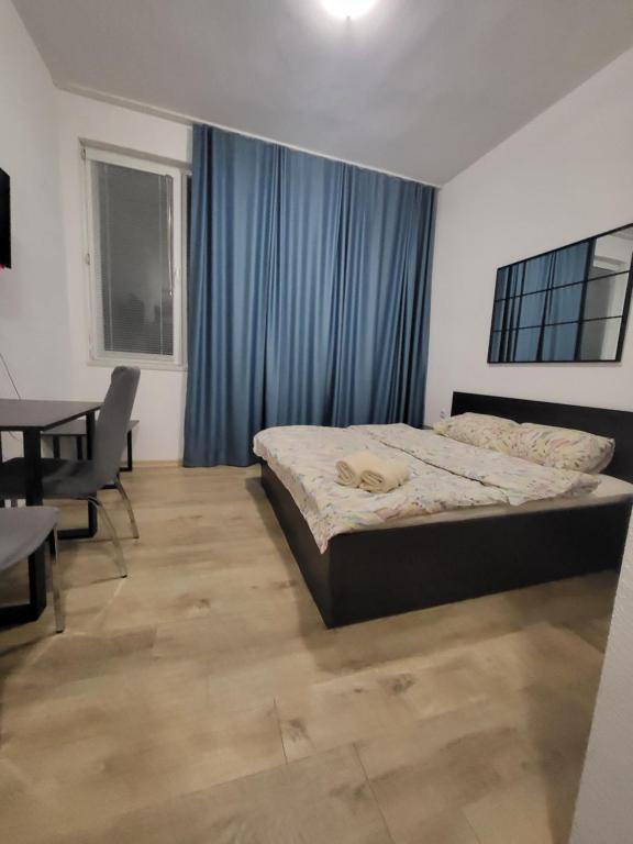 a bedroom with a bed and a table and blue curtains at Стаи за гости Пауза in Stara Zagora