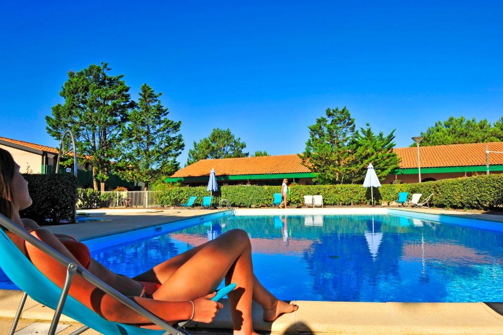 a woman sitting in a chair next to a swimming pool at VTF La Forestière in Lacanau-Océan