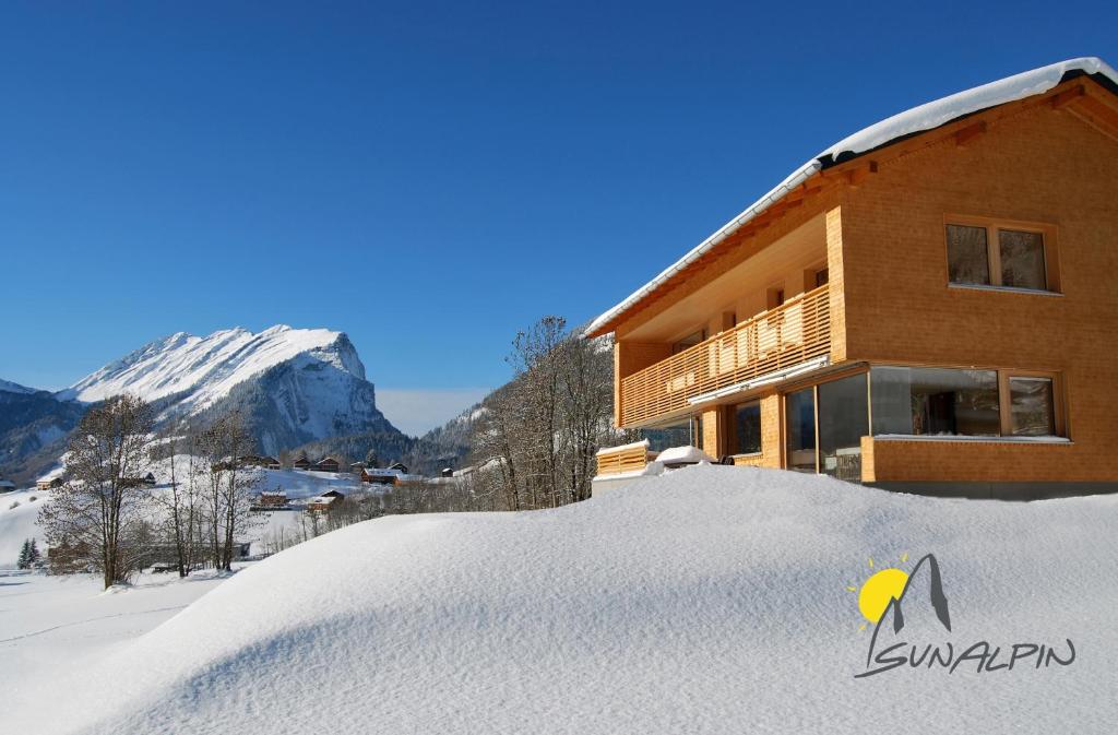 ein schneebedecktes Gebäude vor einem Berg in der Unterkunft SunAlpin - Ferienwohnungen in Schoppernau