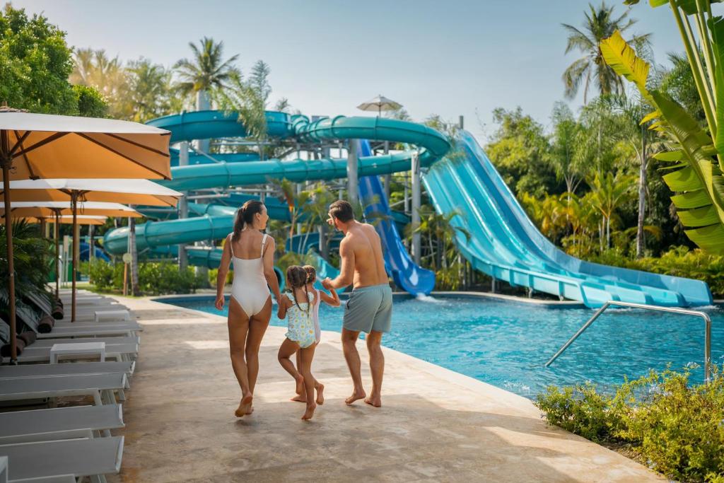 Family entering waterpark area with large blue water slides and shallow pool below.