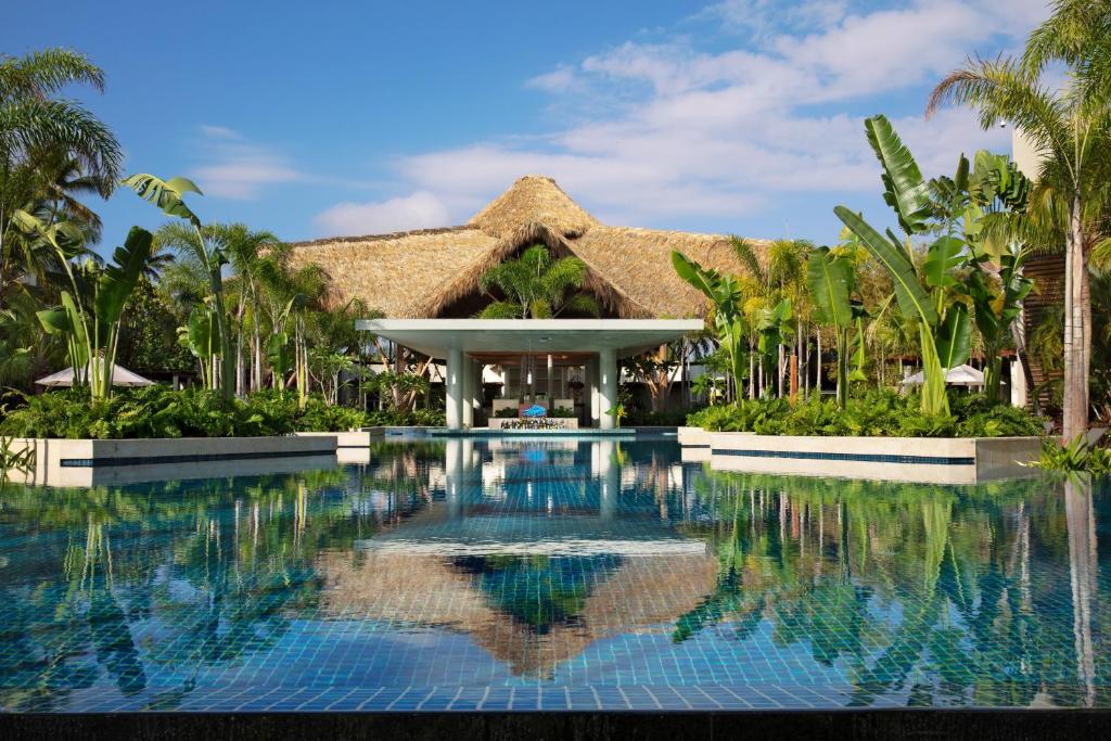 Resort pool with thatched-roof structure, palm trees, and lounge chairs.