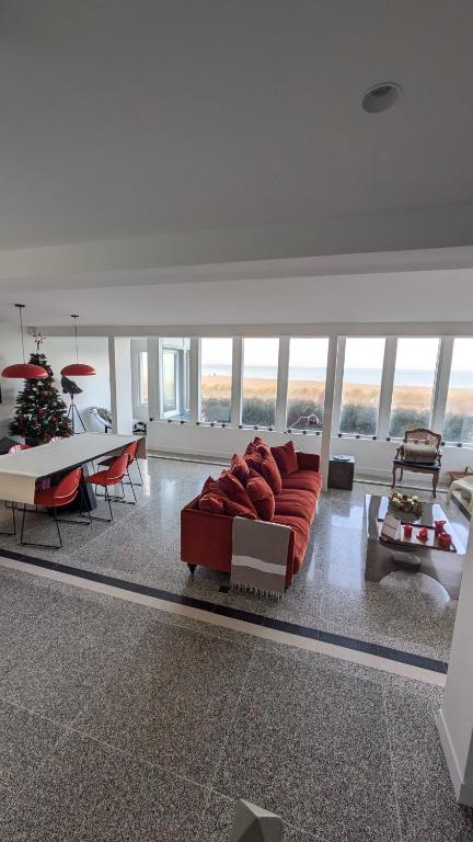 un grand salon avec un canapé rouge et des tables dans l'établissement Villa Bagatelle, 8 personnes front de mer Houlgate, à Houlgate