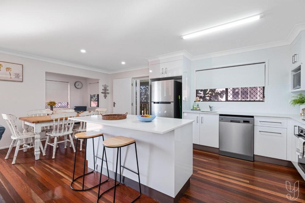 eine Küche mit weißen Schränken und eine Kücheninsel mit Barhockern in der Unterkunft 3 Bedroom Family-Friendly Coastal Haven! in Yeppoon