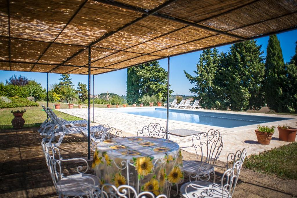 a table and chairs under a pergola next to a swimming pool at Agriturismo Collosodo in Monticchiello