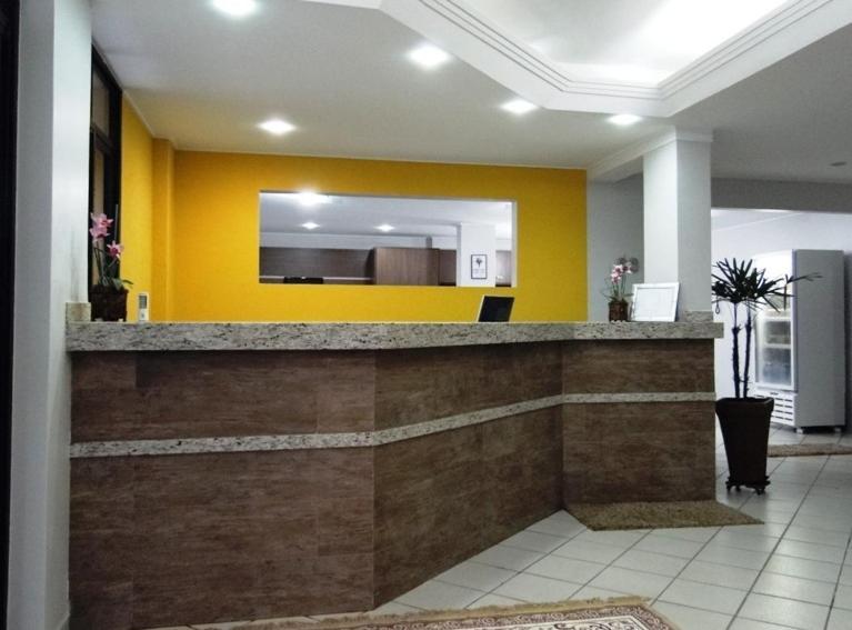 a lobby with a counter with a yellow wall at Paradise Hotel in Campo Grande