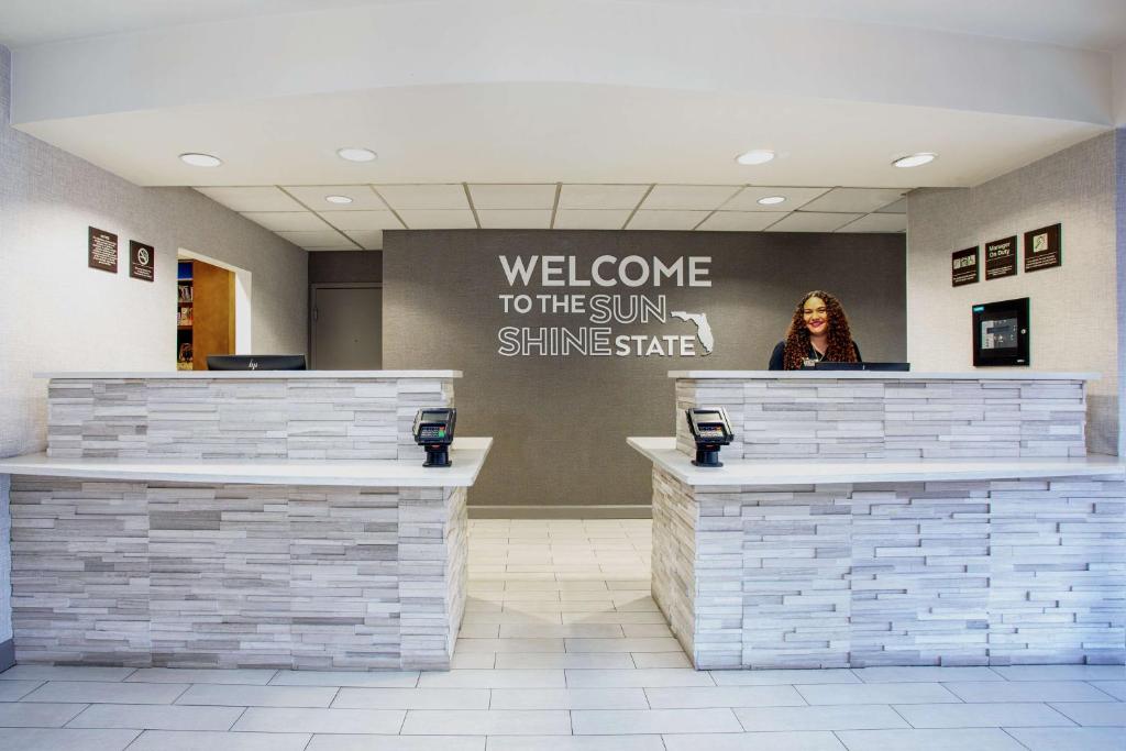 a woman standing at the counter of a welcome to the sun shining shine at Hampton Inn Orlando-International Airport in Orlando